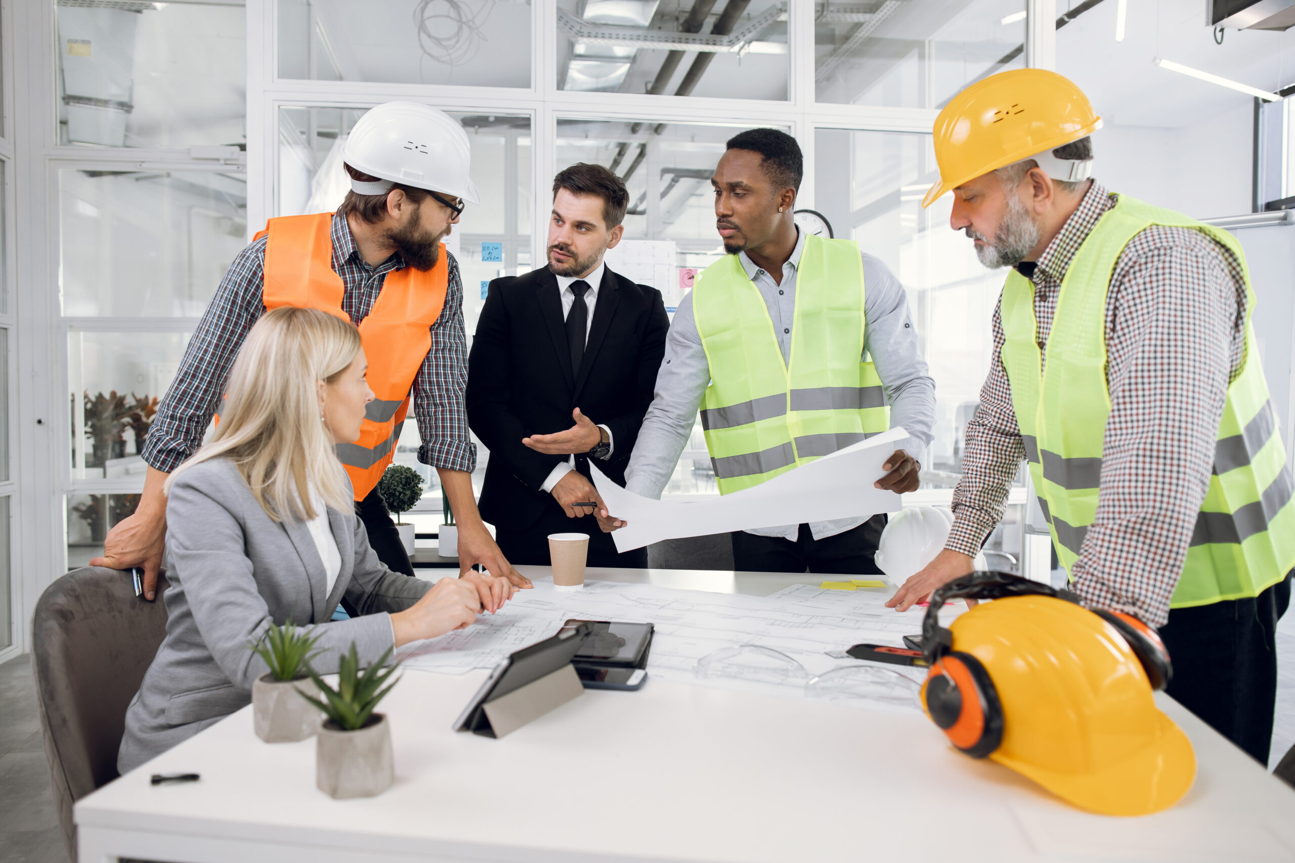 Four bearded men and one beautiful woman spending working time at office for brainstorming of common project. Construction team creating plan of modern building.